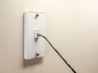 Landline telephone wall mounted jack plate with phone cord.