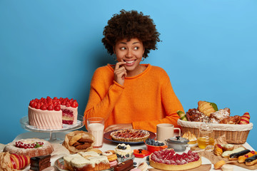 Charming female sweet tooth looks with smiles aside, thinks about something while poses at birthday...