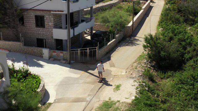 Aerial shot follows skateboarder on narrow paved road in Croatia