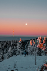 Colorful sunset mountain panorama view in the winter season with snow and full moon rising over the mountain tops with blue sky. Harz Mountains National Park in Germany	