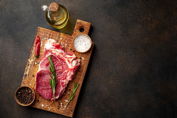 one raw steak with spices and rosemary on a stone background with copy space for your text