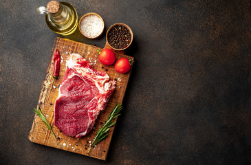 one raw steak with spices and rosemary on a stone background with copy space for your text