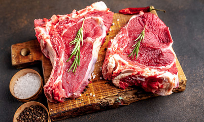 raw beef steaks with spices and rosemary on a stone background