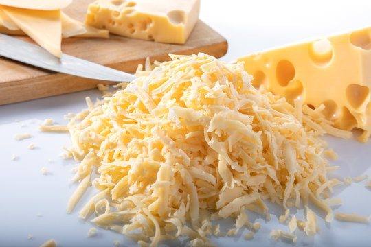 Pieces of Swiss cheese and grated cheese with a knife and a wooden board