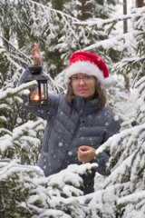 Fototapeta na wymiar young woman in glasses and in a Christmas red cap with a lantern in her hands is happy winter snowfall in the forest among fir trees and snowflakes