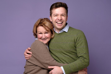 Happy mother and her son hugging standing at studio on colored background. Studio shot