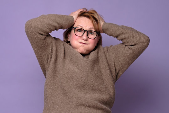 Caucasian Senior Woman In Glasses Too Old For Such Nerves. Concerned And Confused Troubled Senior Lady Holding Hands On Head In Panic. Studio Shot