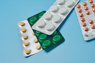 Scattered pills in blister packaging lies on blue desk. Concept of healthcare, drug addict or chemical weapon. Close-up
