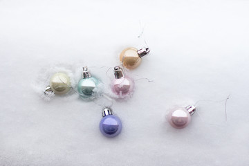multicolored cute little Christmas shiny balls lie in white fluffy snow, top view