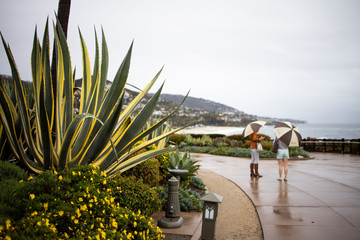 Two Girls with Umbrellas Walking by the Ocean