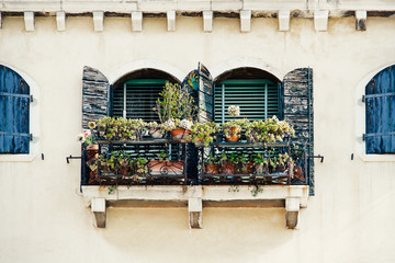 Fototapeta na wymiar windows with blue shutters and flowers on the yellow facade in old house in Venice
