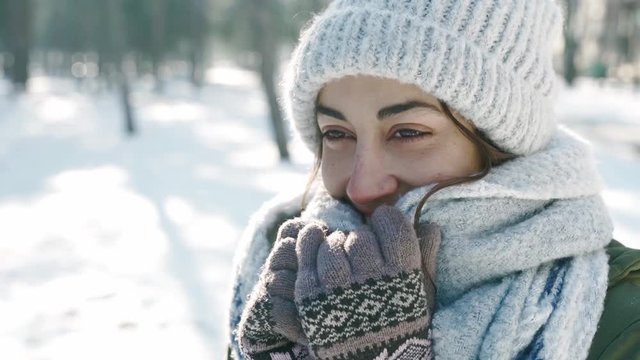 extreme closeup portrait of beautiful smiling woman in woolen cap and long warm scarf in snowy winter park at frozzy sunny day. woman looks playful and wraps herself in a scarf. Happy winter time