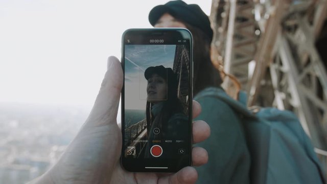 Male hand is filming smartphone video of happy smiling woman posing on top of Eiffel Tower. Romance concept slow motion.