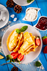 Crepes with strawberries and jam on wooden table