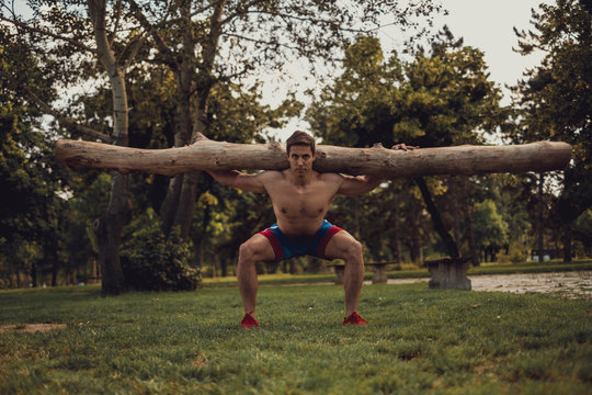 Shirtless man doing squats with hood log on his back