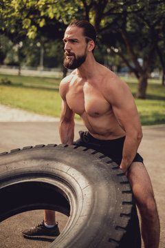 Bearded muscled hipster training with tire in the park