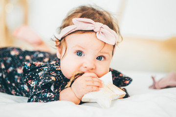 Beautiful baby girls with a bow on her head chews wooden stars. Six month baby girl chewing wooden...
