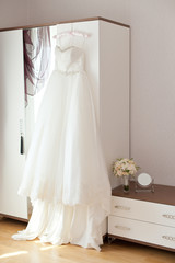 Bridal accessories: wedding dress, shoes and bride's bouquet in a loght room. Bride's room in wedding day