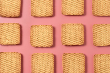 Rows of many whole square cookies lies on pink desk on kitchen. Close-up