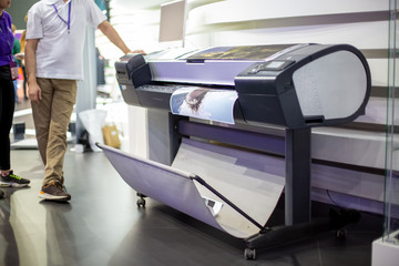 plotter prints a poster. standing next to people in blur. close-up, background in blur