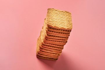One heap of whole square cookies lies on pink desk on kitchen. Close-up