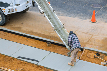 Worker freshly poured concrete mix concrete from the cement mixer in sidewalk