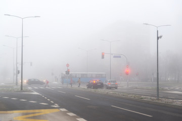 City crossroads with stoplights and pedestrians in the fog