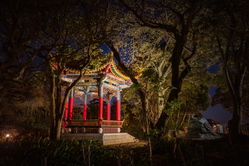 Fototapeta premium Japan. Island Fujisawa. Kanagawa Prefecture. Traditional Japanese building in the Park. Illuminated Japanese gazebo among dark trees. Travelling to Japan. Sights Of Japan.