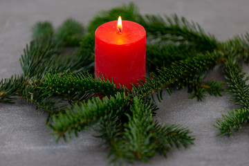 Christmas motif, texture, background with branches of a Nordmann fir and burning red candle on a dark grey marbled  background.