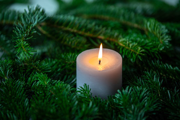 Christmas motif, texture, background with branches of a Nordmann fir and burning white candle on a dark grey marbled  background.