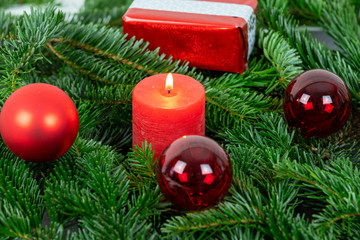Christmas motif with red burning candle surrounded by Nordmann fir branches, red christmas tree balls and gift parcel