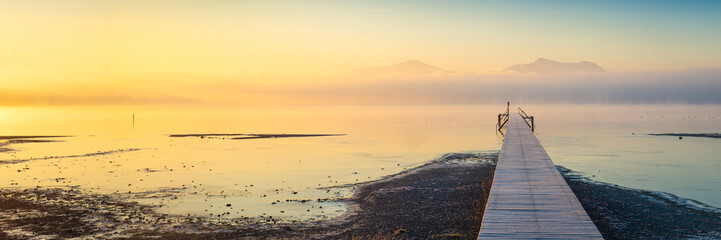 Fototapeta premium Sonnenaufgang am See mit Steg und Nebel - Chiemse Panorama