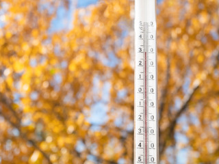Naklejka na ściany i meble Outdoor thermometer close-up on a background of blurred yellow trees. 30 degrees heat.