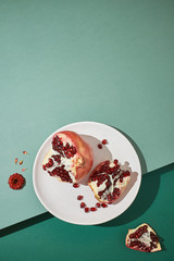 Sliced pomegranate on a plate on a green background. Flat lay and copy space