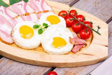 Tasty fried eggs with vegetables on a wooden plate.
