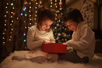 Family on Christmas eve at fireplace. Kids opening Xmas presents. Children under Christmas tree...