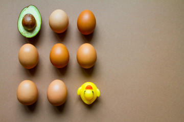 One half of row avocado, few chicken eggs and yellow rubber duck on a brown background, flat, top view