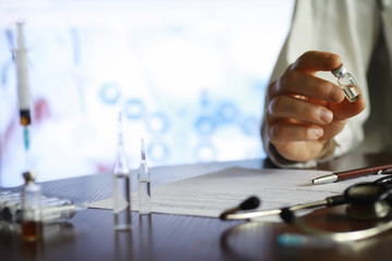 A man signs a medical document. Medical equipment on the table. Stethoscope and ampoules with syringes. Makes notes in the office. Medical center.