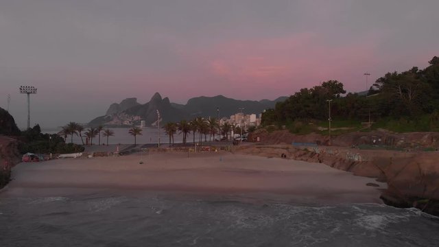 Aerial approach on Devils beach at the Arpoador in Rio de Janeiro with Ipanema and Leblon in the background at early morning sunrise against a magenta sky from the sunrise