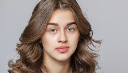 Fototapeta premium Portrait of a beautiful happy woman with curly hair, clean skin and thick eyebrows beauty salon. Eyelash extensions. Face close-up. Make-up concept.