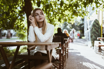 Fototapeta premium lovely blonde looks thoughtfully at the side resting her cheek on her hands in an outdoor cafe