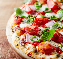 Pizza with ham, cherry tomatoes, mozzarella cheese, jalapeno pepper and fresh herbs. Close up.