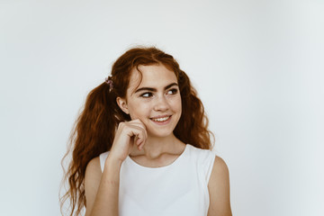 a cunning and mischievous look of a girl with tails of red very thick and long hair. gray background