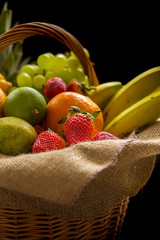 Fruit Basket with banana, oranges, pears, ananas, grapes, strawberries, lime and apples isolated on a black background