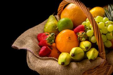 Fruit Basket with banana, oranges, pears, ananas, grapes, strawberries, lime and apples isolated on a black background