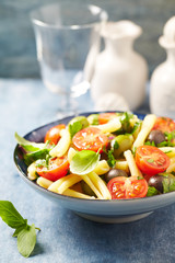 Casarecce pasta with cherry tomatoes, kalamata olives and fresh herbs. Bright wooden background.