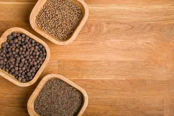 Cumin, coriander and pepper in bamboo jars on a wooden background. Top view with copy space.