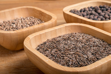Cumin, coriander and pepper in bamboo jars on a wooden background.