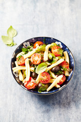 Casarecce pasta with cherry tomatoes, kalamata olives and fresh herbs. Bright wooden background. 