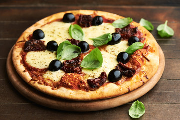 Pizza with mozzarella cheese, marinated tomatoes, black olives and fresh basil. Rustic wooden background.